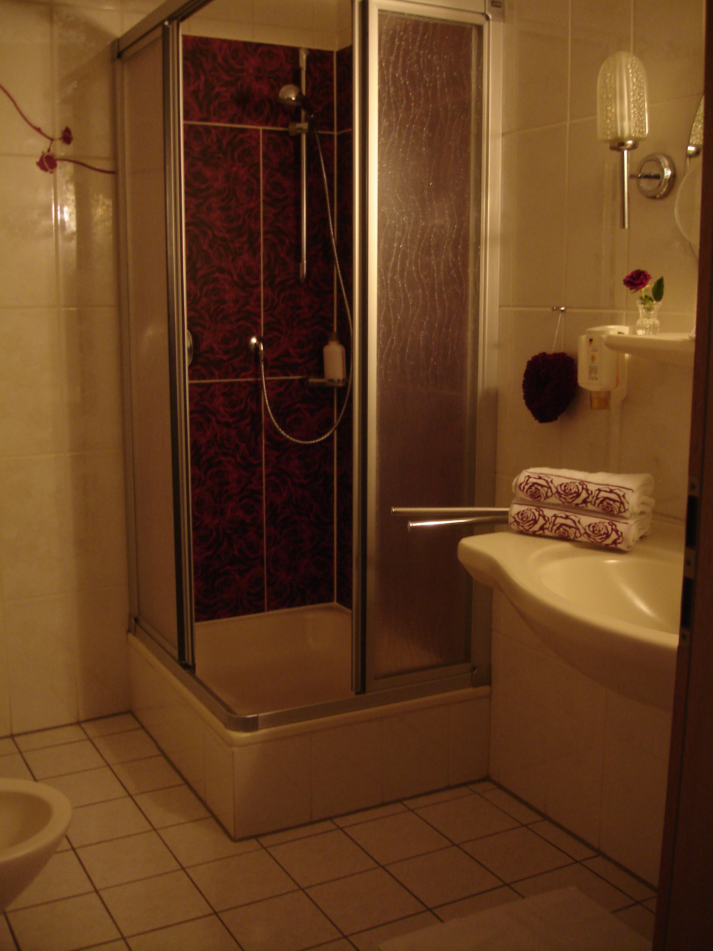 A bathroom with a glass-enclosed shower, a toilet, and a sink with a vase of flowers.