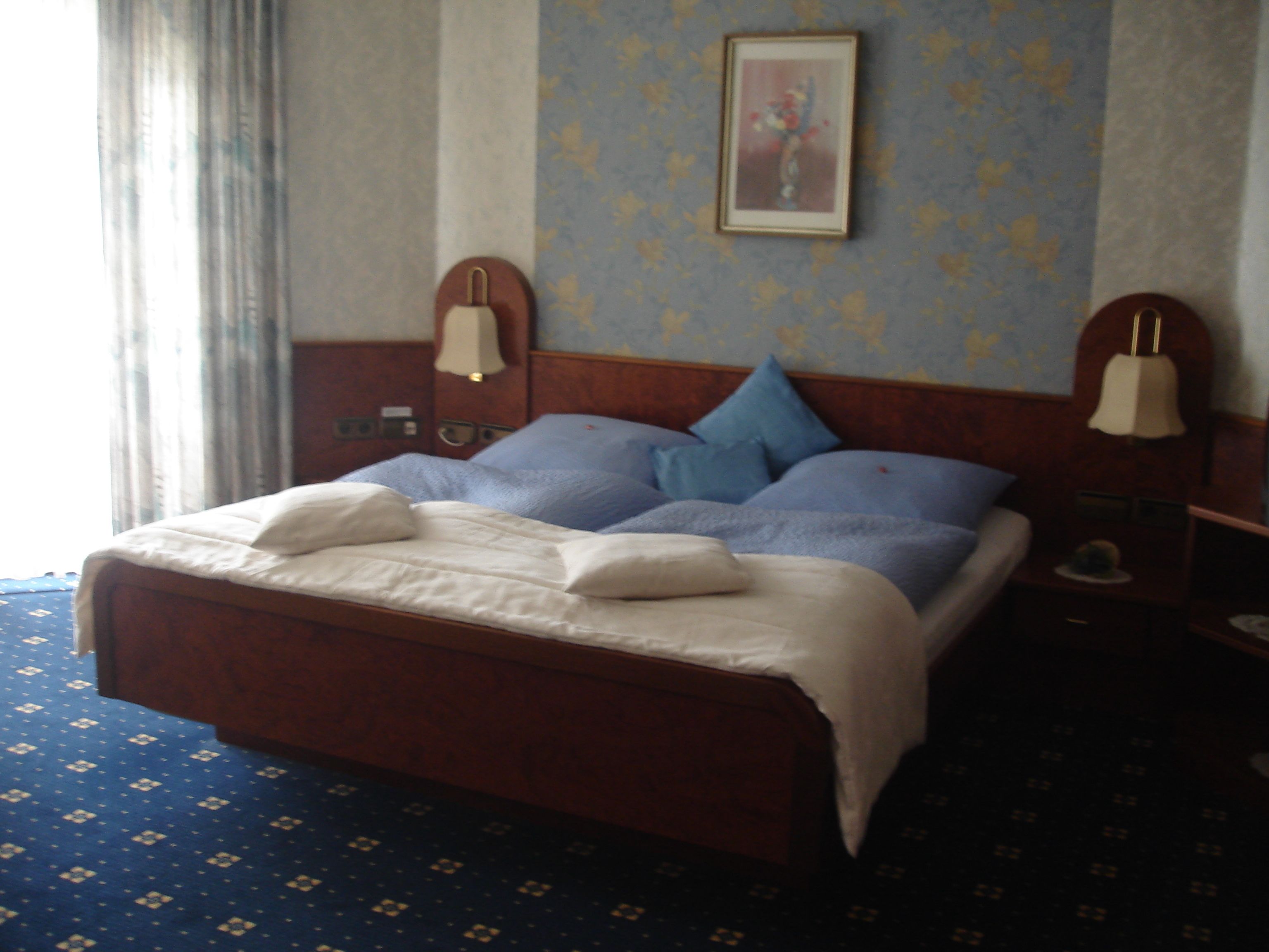 A hotel room with a large bed, two bedside lamps, a painting on the wall, and a patterned carpet.