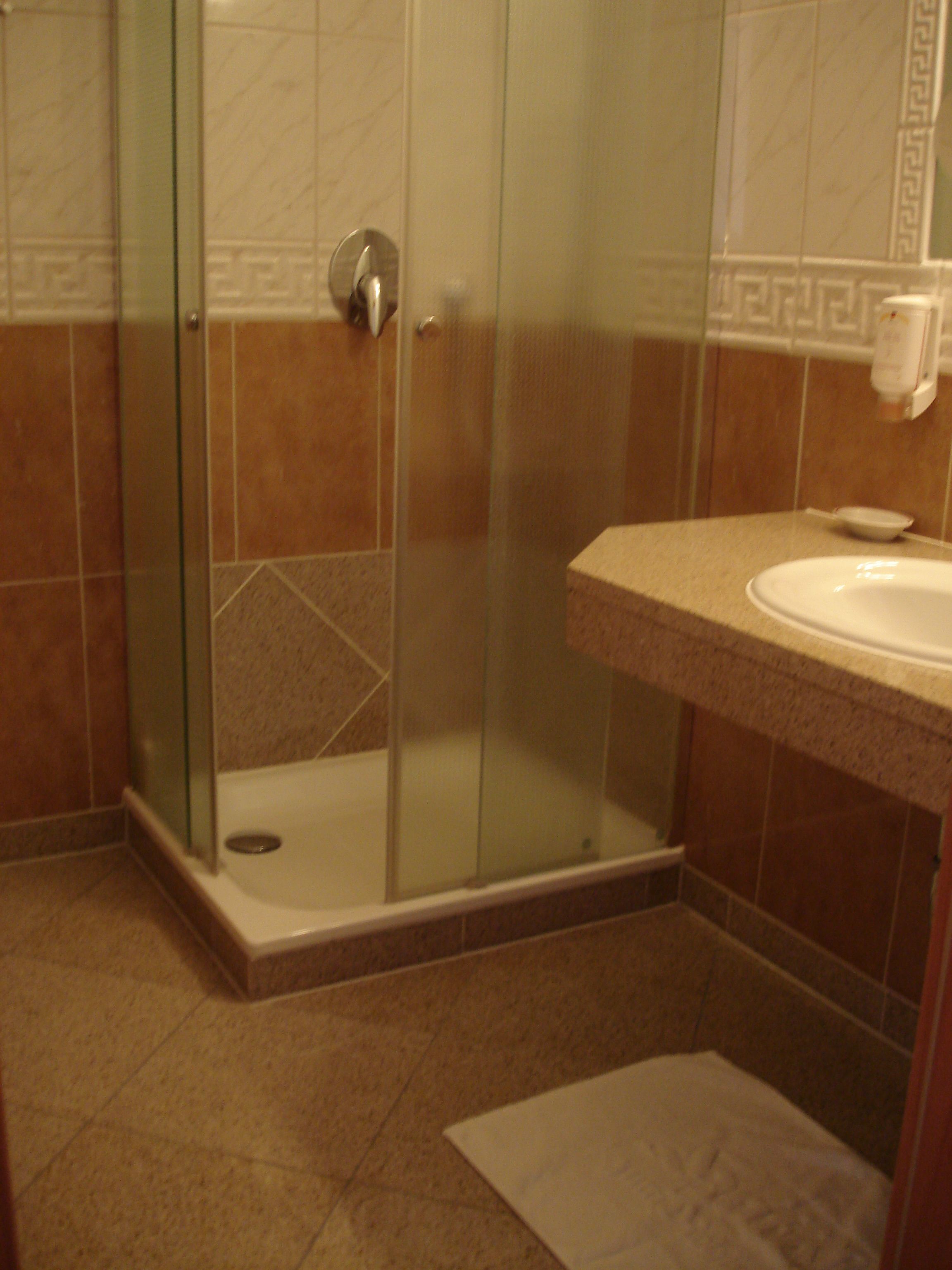 Un baño con ducha de vidrio, un lavamanos y un perchero para toallas.