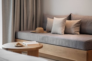 A modern living room with a grey sofa, a round wooden coffee table, and a woven hat on the sofa. - Magda Hotel (Hersonissos)