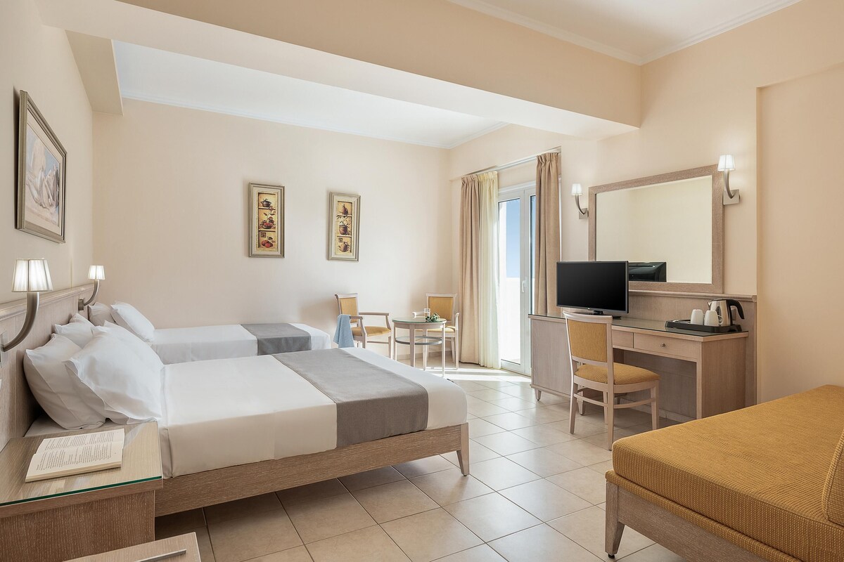 A hotel room with two beds, a desk with a computer, a chair, a TV, and a large mirror.