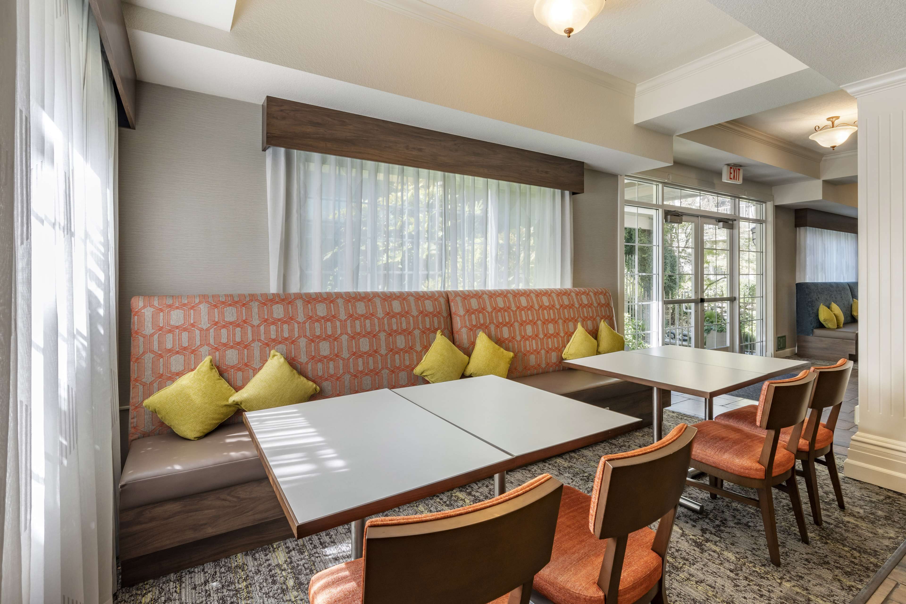 A dining area with a long table, several chairs, a cushioned bench, and a window with curtains.
