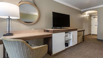 A hotel room with a wooden desk, a television, a chair, and a mirror.