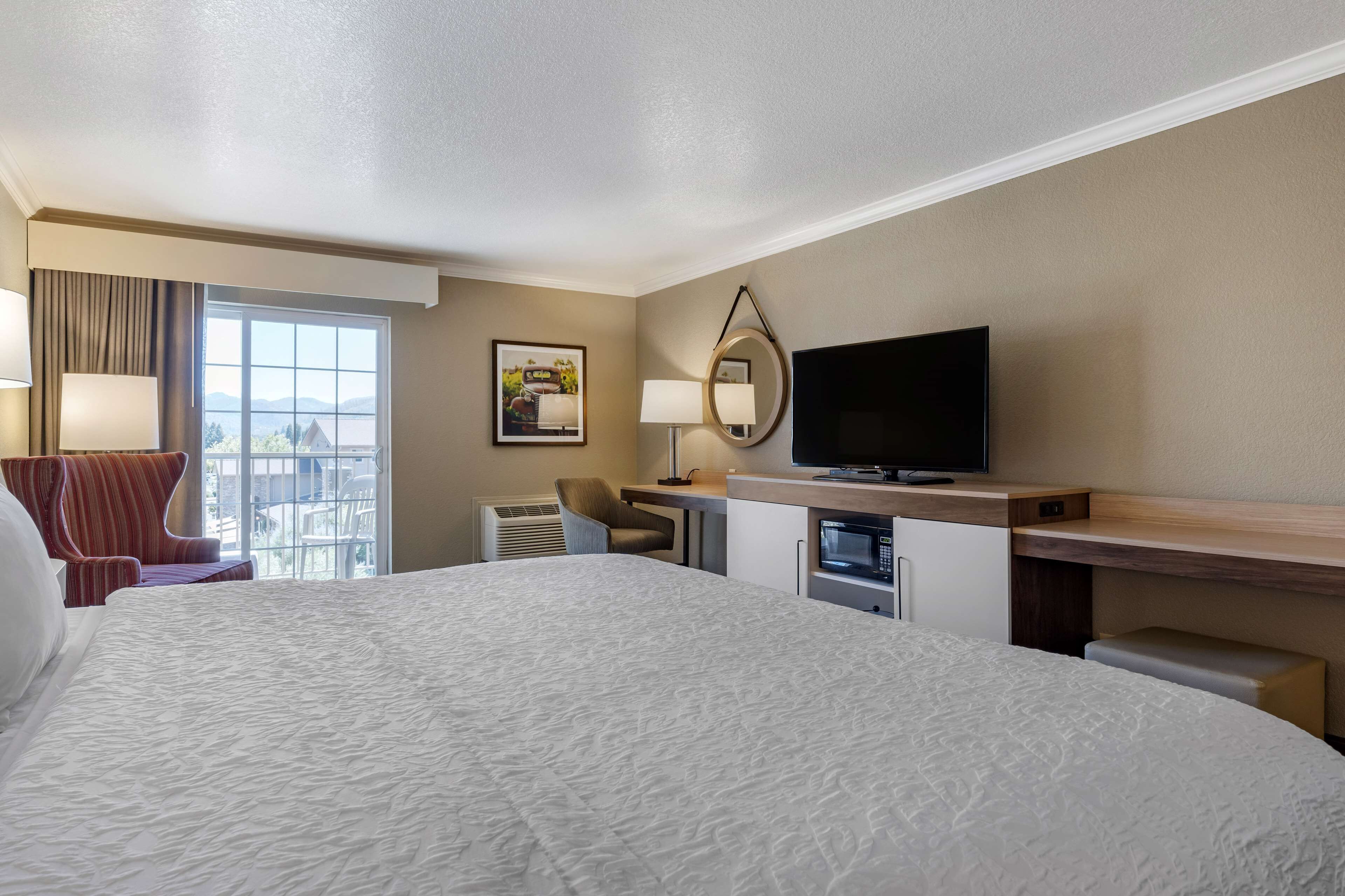 Habitación de hotel con una cama grande, televisión, escritorio con computadora, silla y ventana con vistas al exterior.
