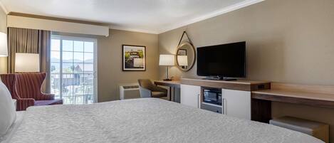 Habitación de hotel con una cama grande, televisión, escritorio con computadora, silla y ventana con vistas al exterior.