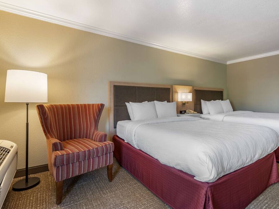 Une chambre d’hôtel avec deux lits, un fauteuil à rayures, une lampe sur pied et un radiateur.