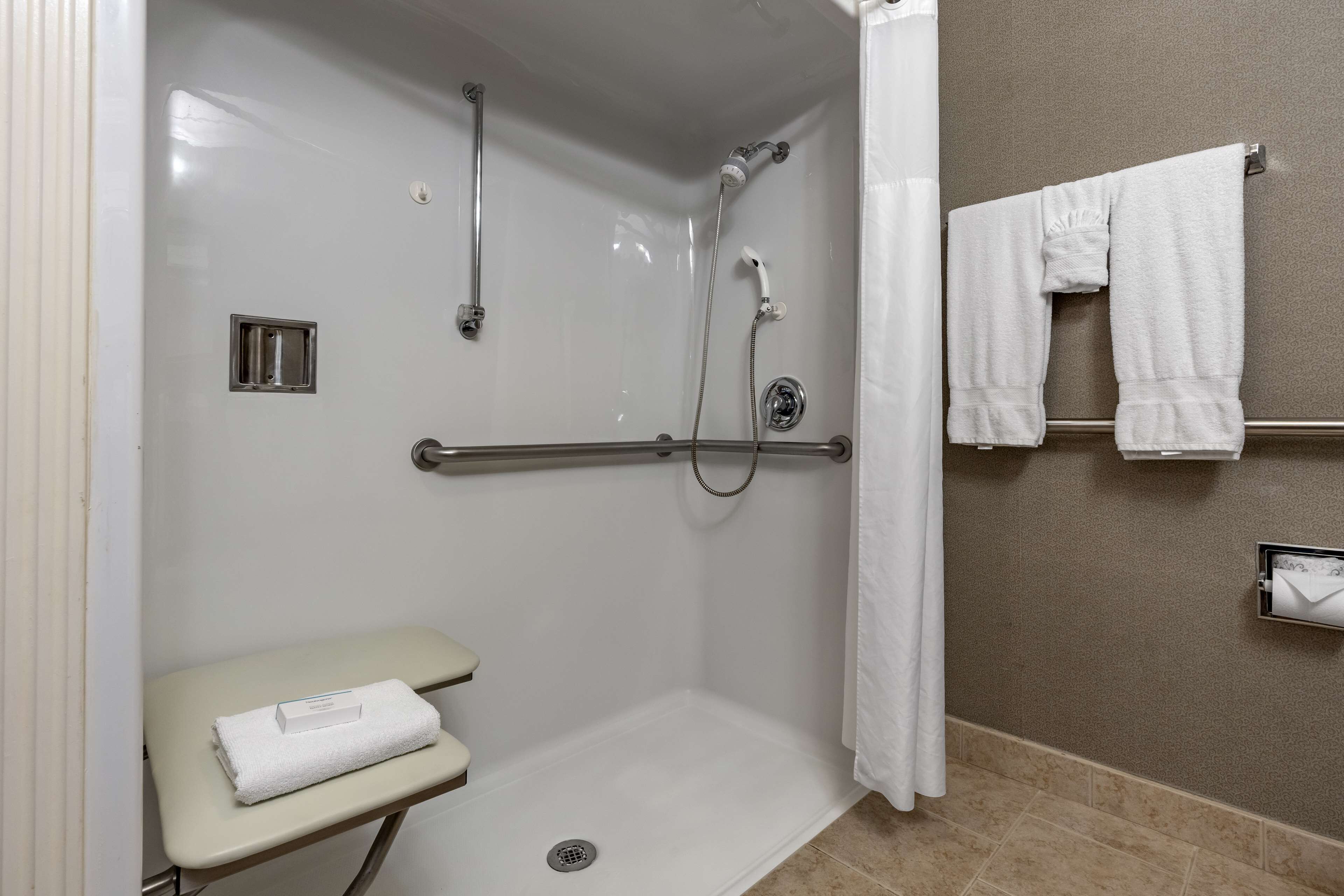 A shower area with a grab bar, a towel rack, and a towel on a bench.