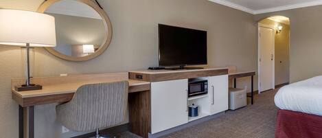 A hotel room with a desk, chair, television, microwave, and a bed.
