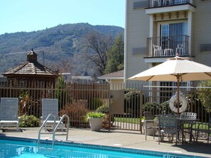 A pool area with a view of a mountain, a gazebo, and a building with a balcony.