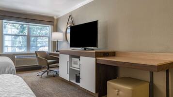 A hotel room with a bed, a desk with a TV, a chair, a lamp, and a suitcase.