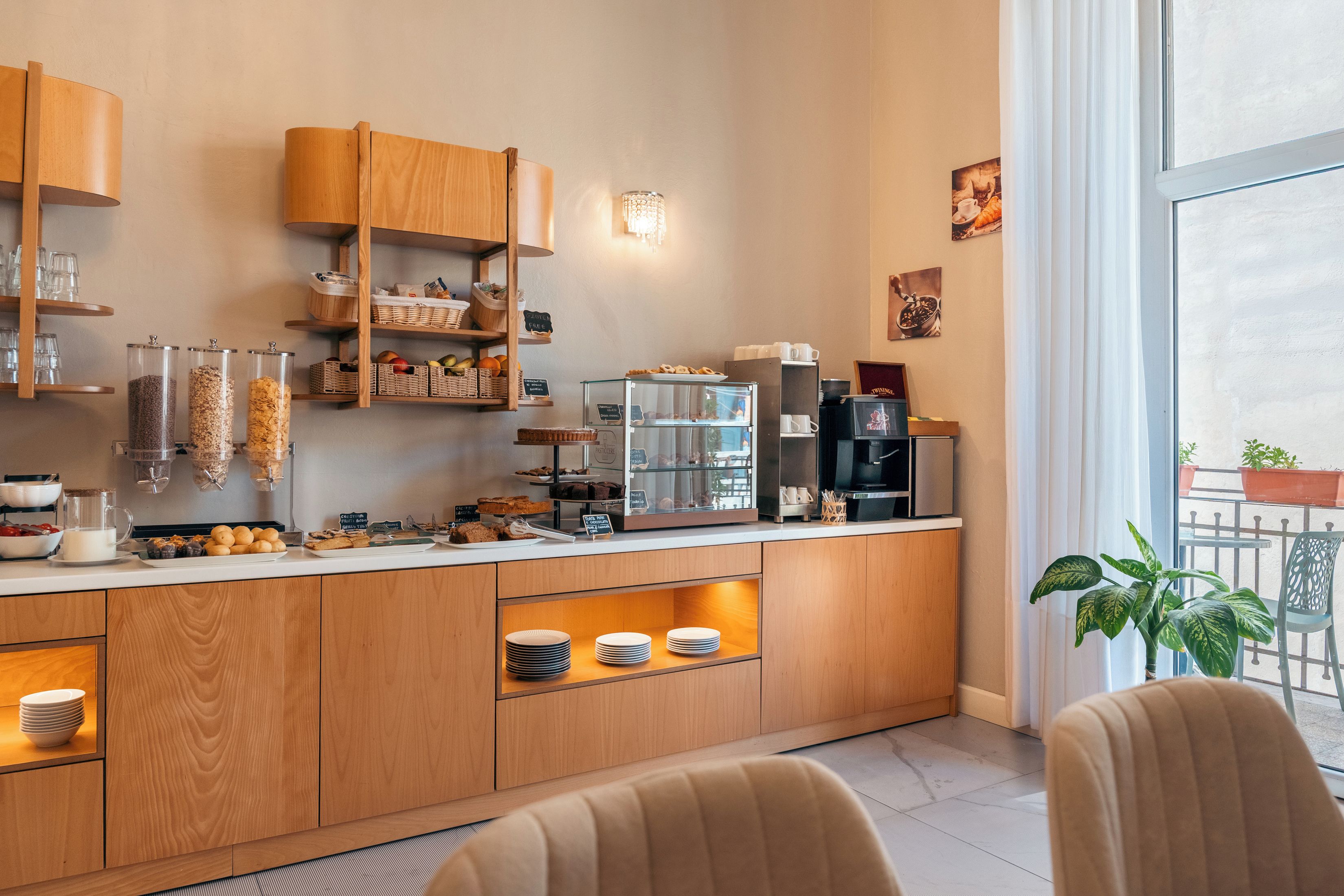 A modern cafe with wooden cabinetry, a coffee machine, and a variety of baked goods displayed on shelves.
