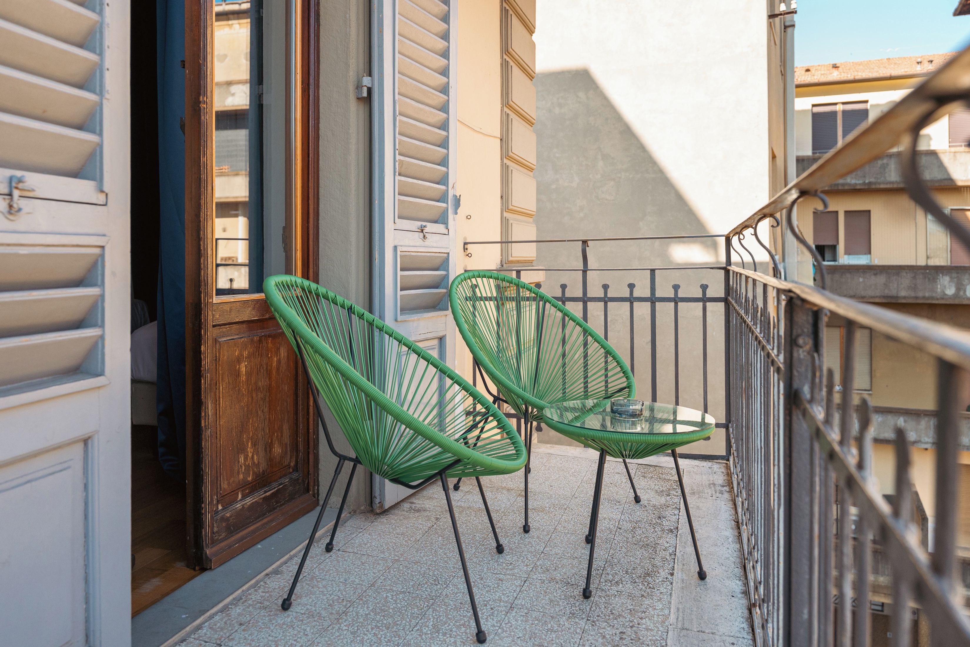 A balcony with two green chairs and a glass table.