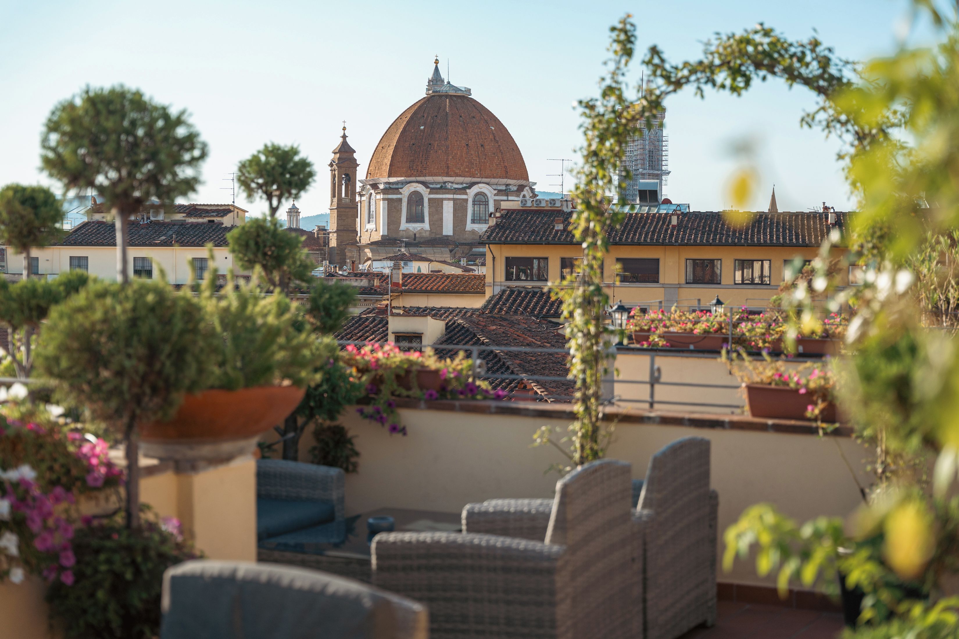 A terrace with outdoor furniture, potted plants, and a view of a historic building with a dome.