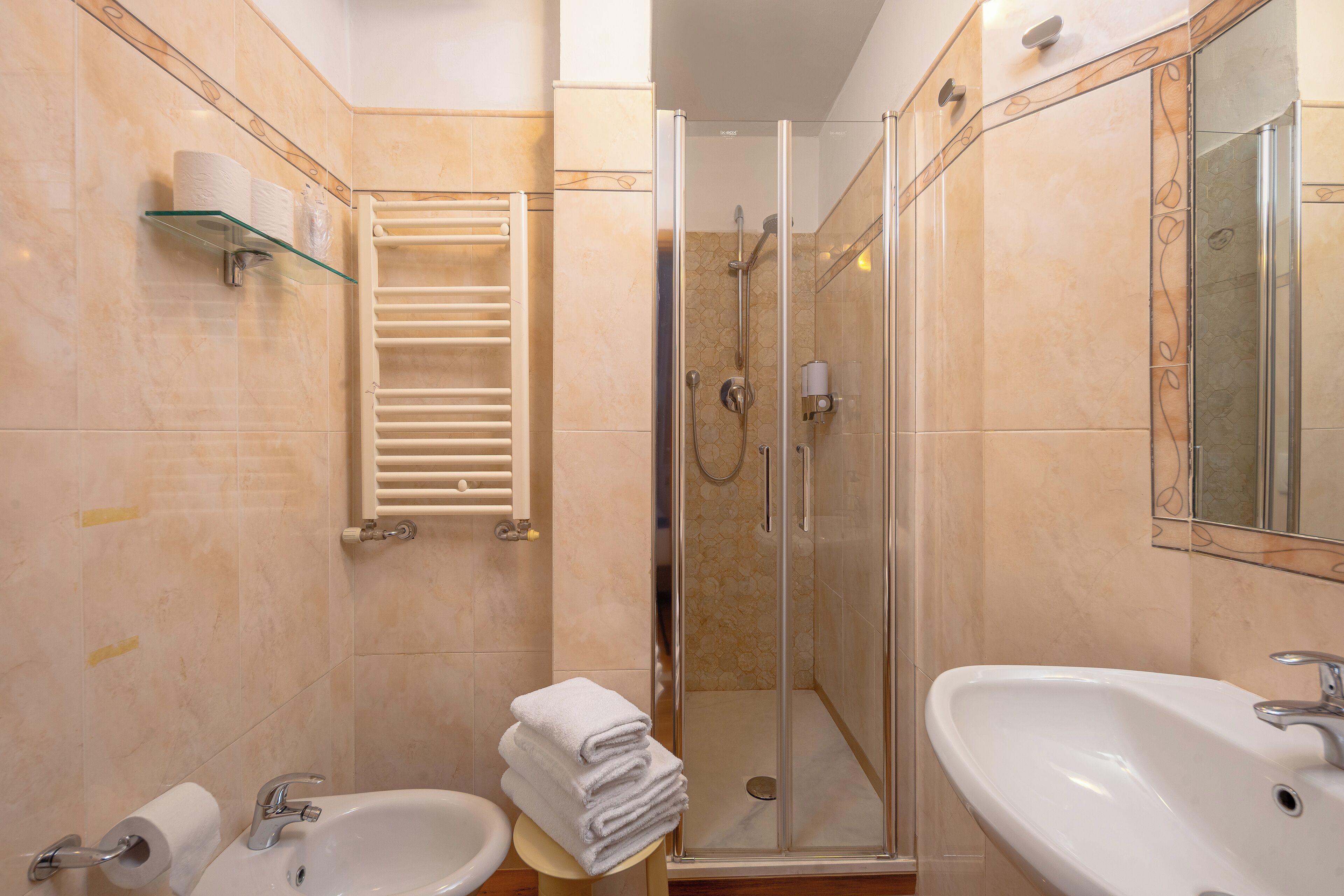 Un baño con dos lavamanos, cabina de ducha de vidrio, toallero y un inodoro.