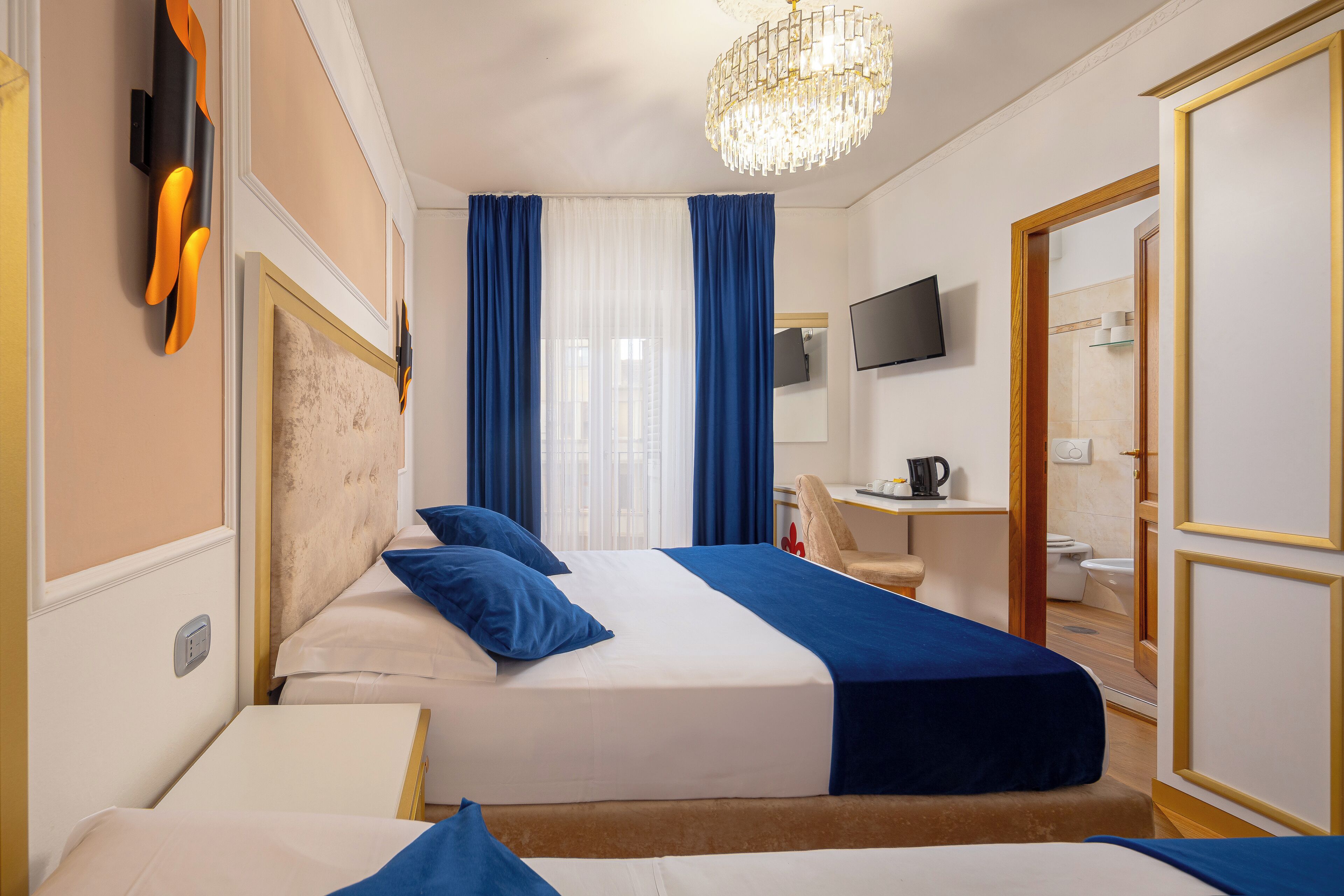 Une chambre d’hôtel avec deux lits, une télévision, un bureau et une salle de bain visible à travers une porte ouverte.