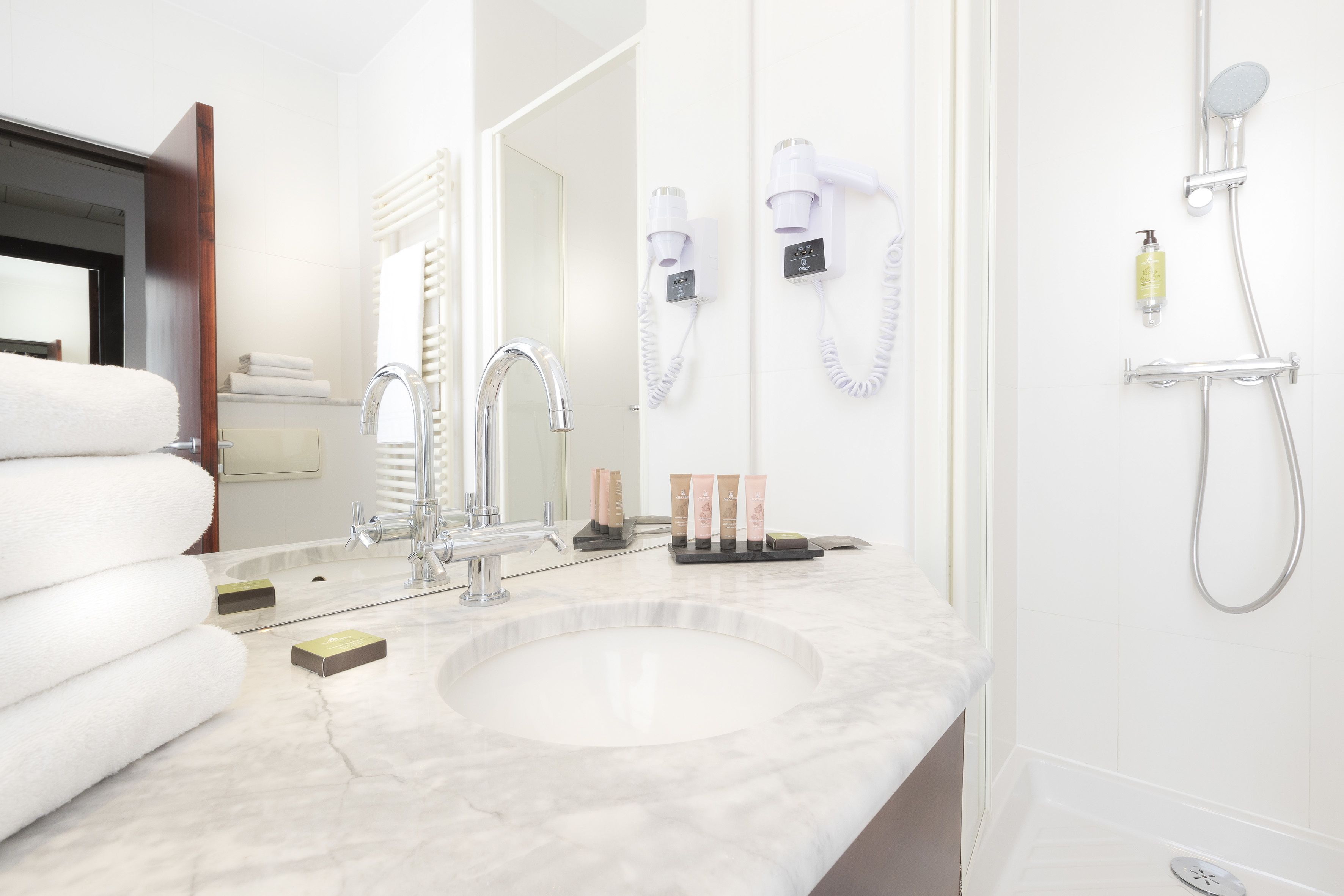 A modern bathroom with a marble sink, a large mirror, a towel rack, a hairdryer, and a shower.