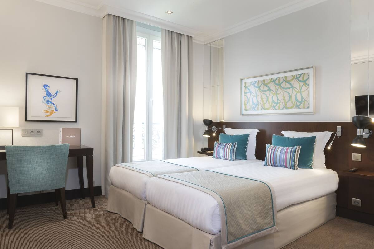 Une chambre d’hôtel avec un grand lit, deux tables de chevet, un bureau, une chaise et des œuvres d’art accrochées aux murs.