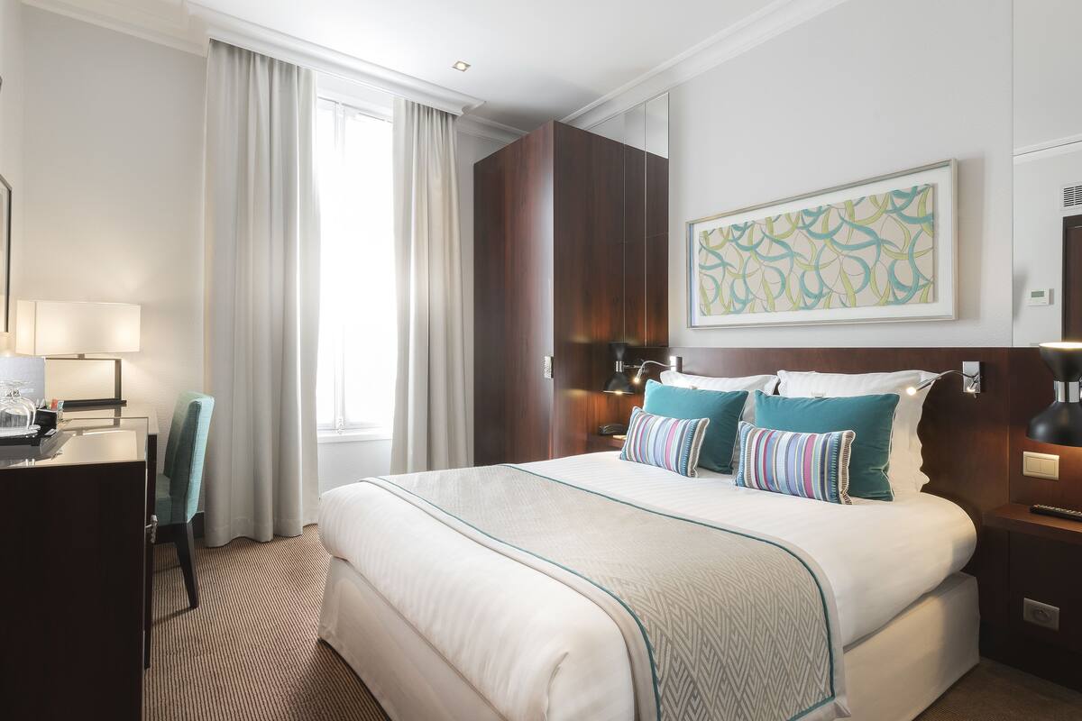 Une chambre d’hôtel avec un grand lit, un bureau avec une lampe, une chaise et un tableau au mur.