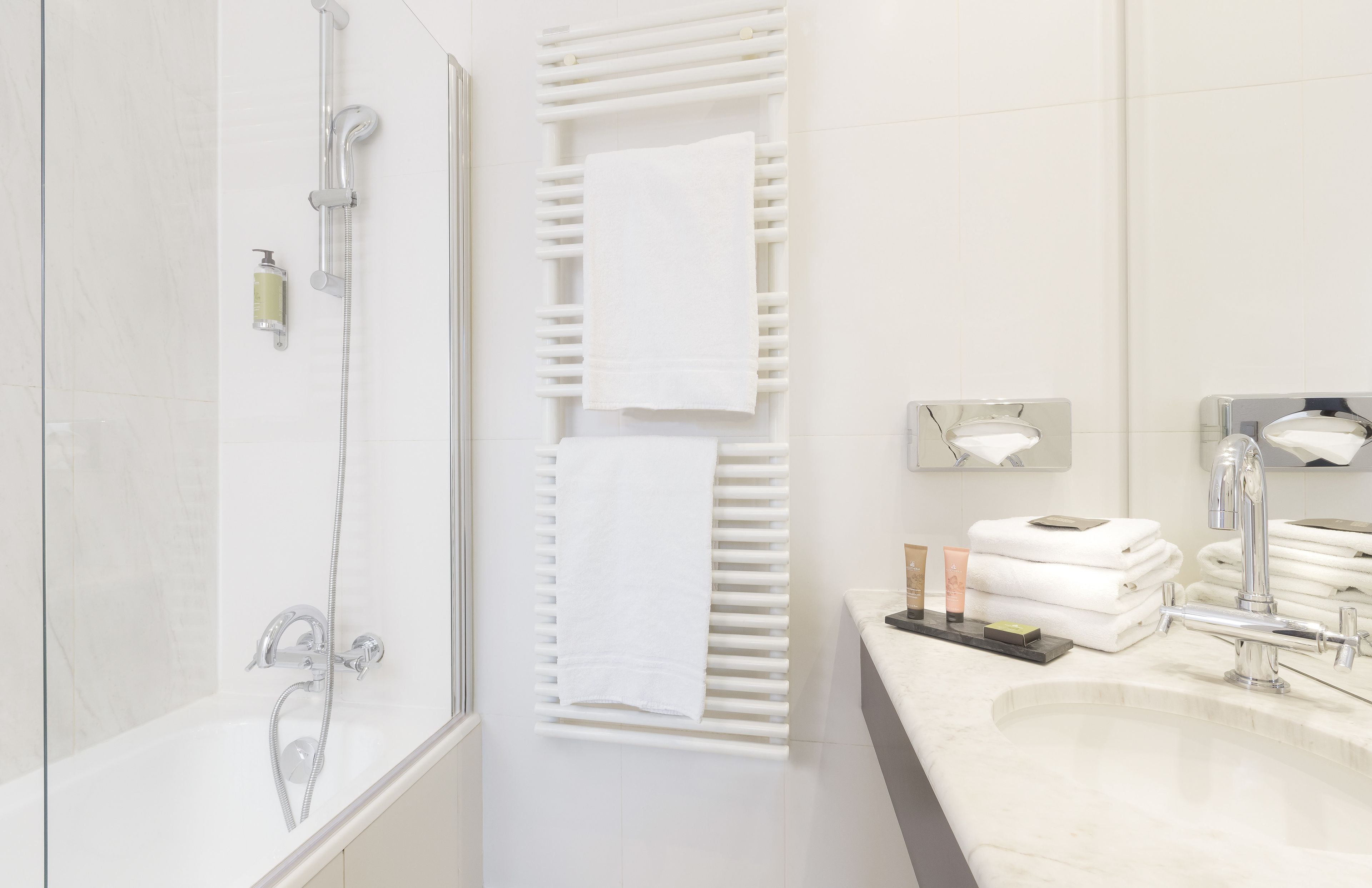 Un baño moderno con ducha envuelta en vidrio, un perchero, un lavabo con espejo y toallas ordenadas.