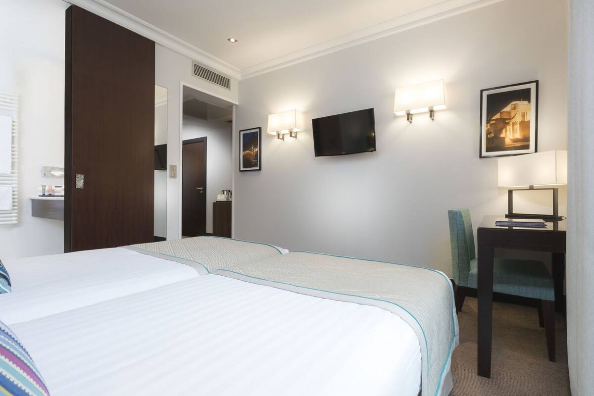 Une chambre d’hôtel avec deux lits, un bureau, une chaise, un téléviseur à écran plat et des lampes fixées au mur.
