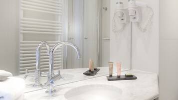 A modern bathroom with a large sink, two hair dryers mounted on the wall, and a towel rack.