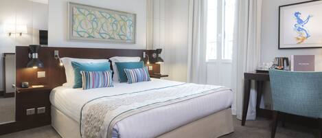 A hotel room with a large bed, bedside lamps, a desk, and a chair.