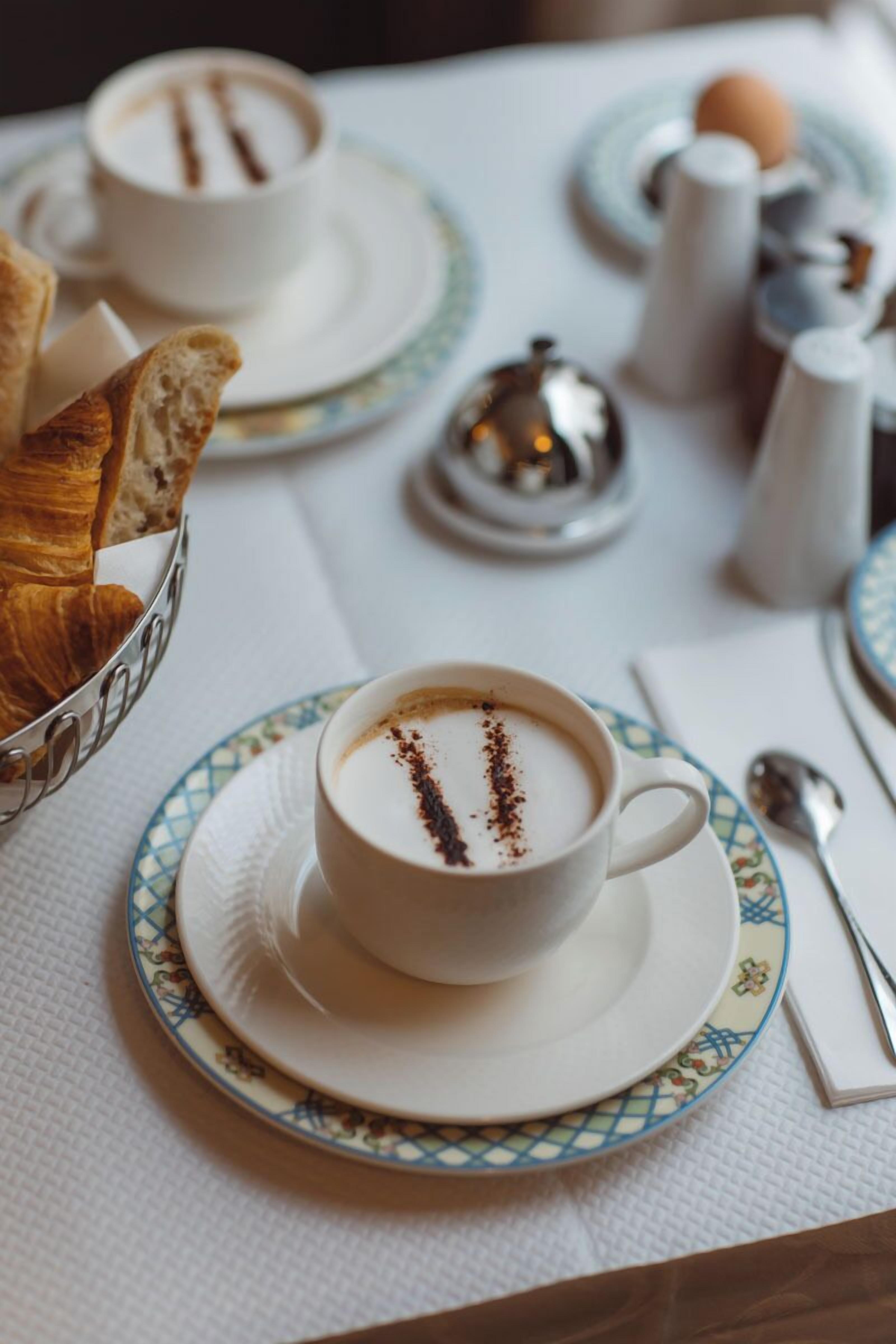 Un desayuno con una taza de café, croissants y salero y pimentero sobre una mesa.
