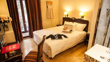 Una habitación de hotel con cama, lámparas de noche, un escritorio con una computadora portátil, una silla y un baño con lavamanos y espejo.