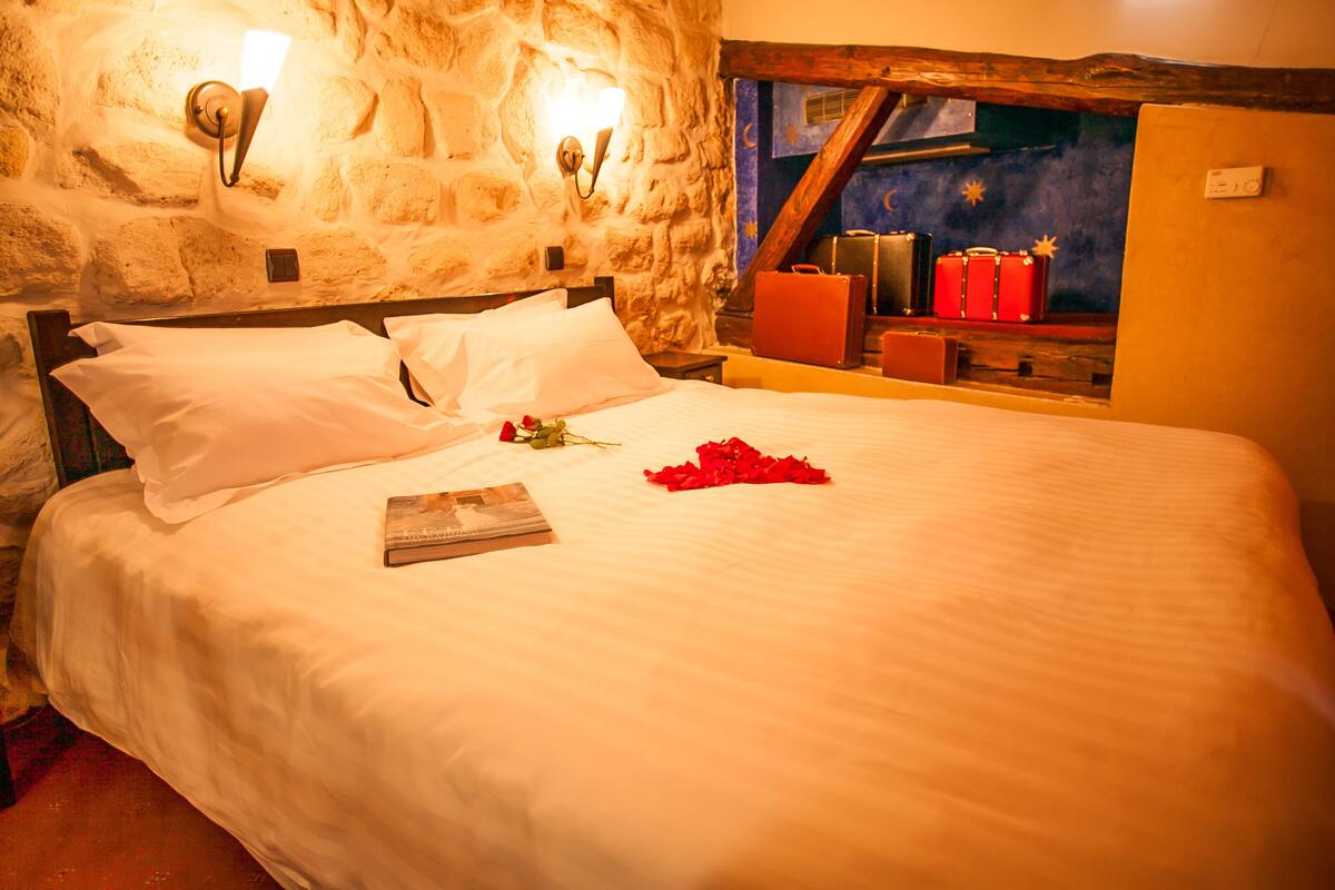 A neatly made bed with white linens, a single rose, and a book on the bed.
