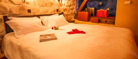 A neatly made bed with white linens, a single rose, and a book on the bed.