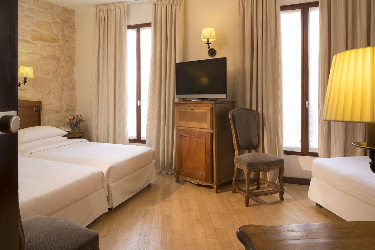 Ein Hotelzimmer mit zwei Betten, einem Fernseher auf einer Holzkommode, einem Sessel und einer Lampe.