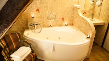 A bathroom with a large bathtub, a wooden chair with a towel, a mirror, and a wall-mounted hairdryer.
