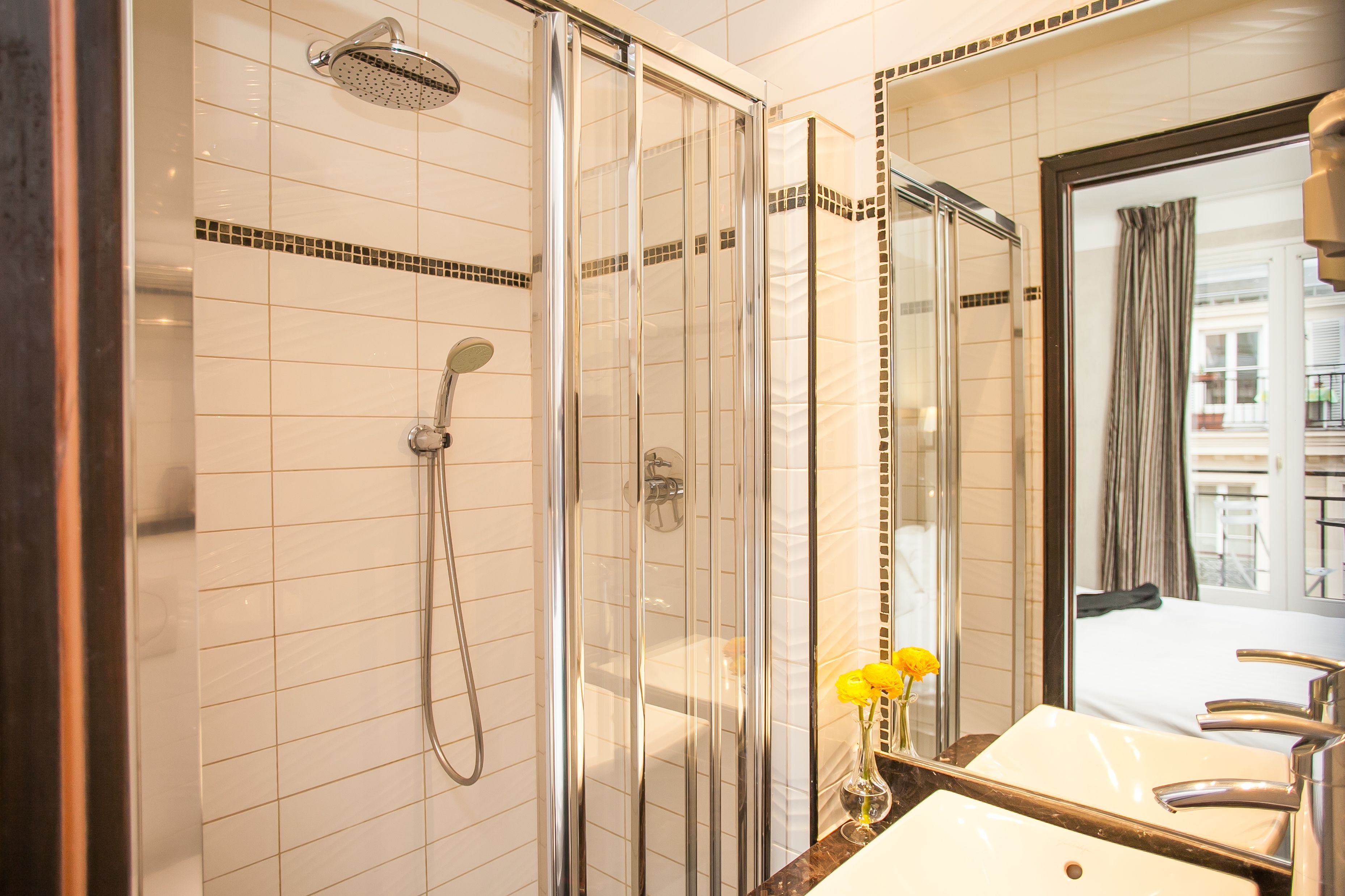 Un baño moderno con ducha de vidrio, un espejo grande y un lavamanos con un florero de flores amarillas.