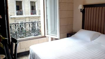 Habitación de hotel con cama, ventana con vista a un edificio, una mesita y una silla.
