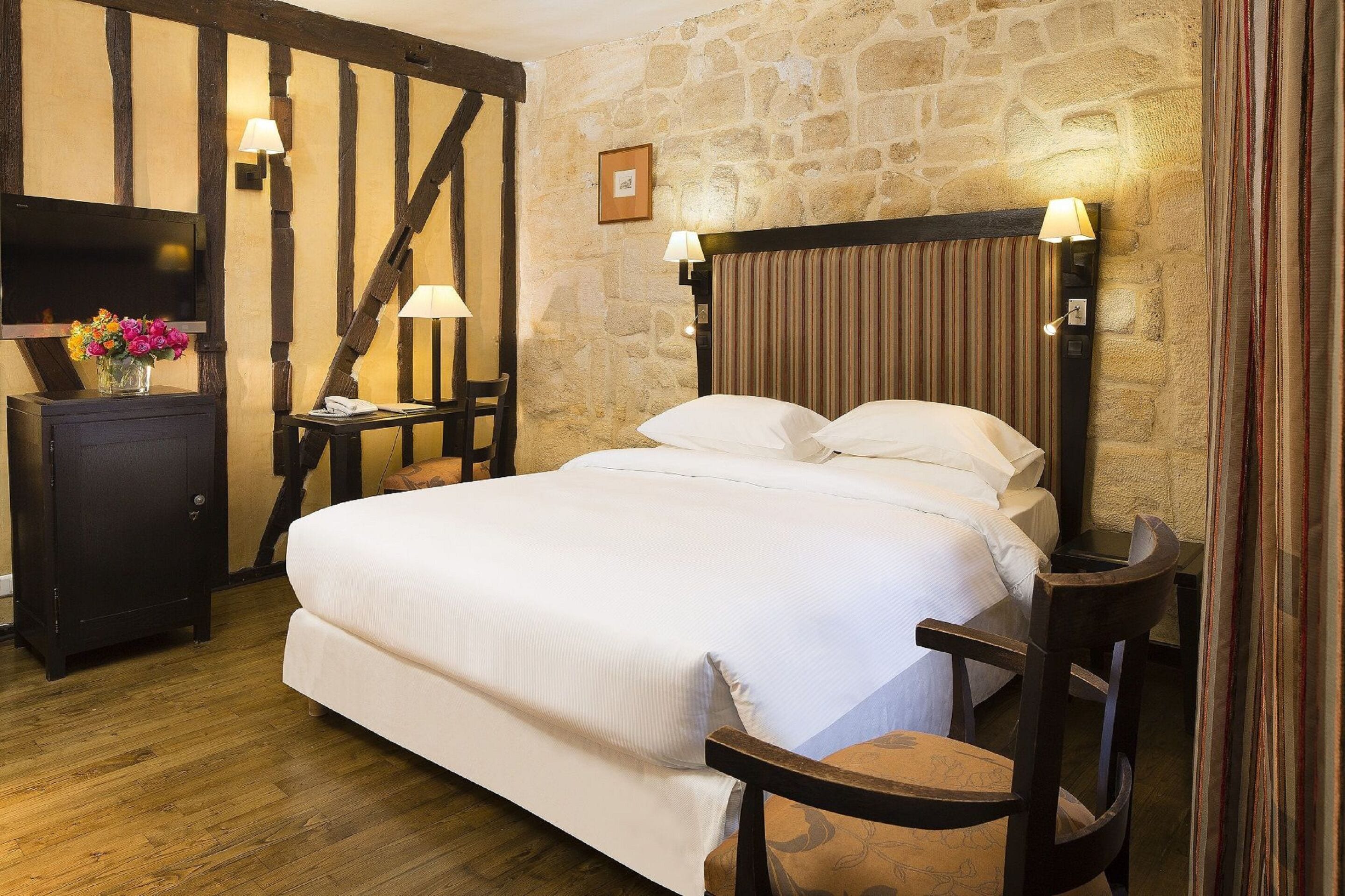 A bedroom with a large bed, wooden headboard, stone wall, and a television on a cabinet.