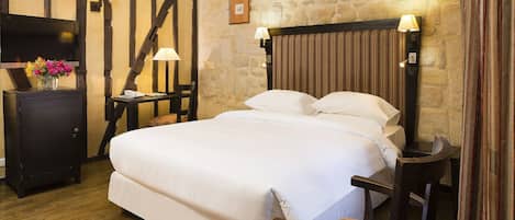 Un dormitorio con una cama grande, cabecera de madera, pared de piedra y un televisor sobre un mueble.