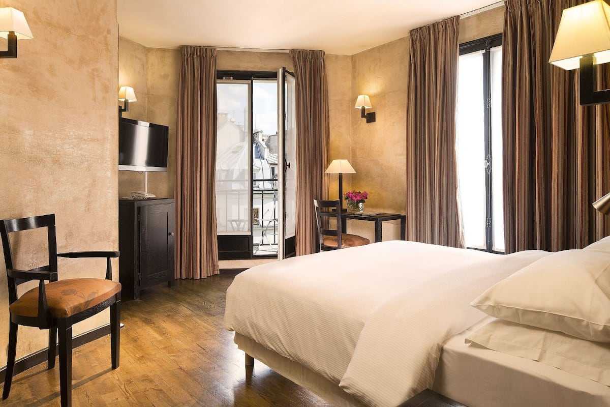 Ein Hotelzimmer mit Bett, Schreibtisch, Stuhl, Fernseher und einem Balkon mit Vorhängen.