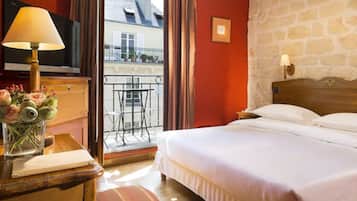 A hotel room with a bed, a desk with a lamp, a TV, and a view of the outside balcony.