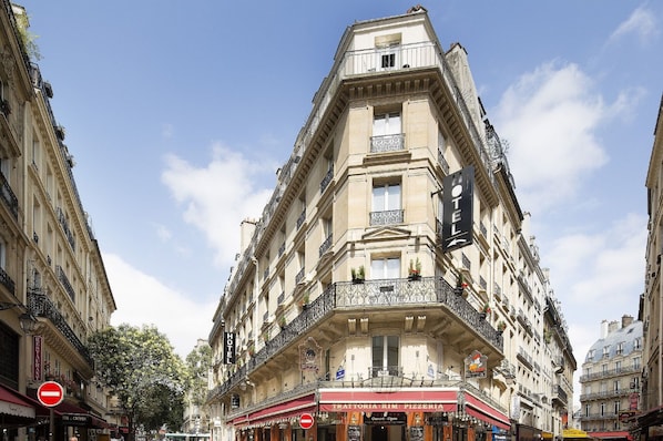 Un edificio en esquina con cartel de hotel, restaurante y pizzería en la planta baja.