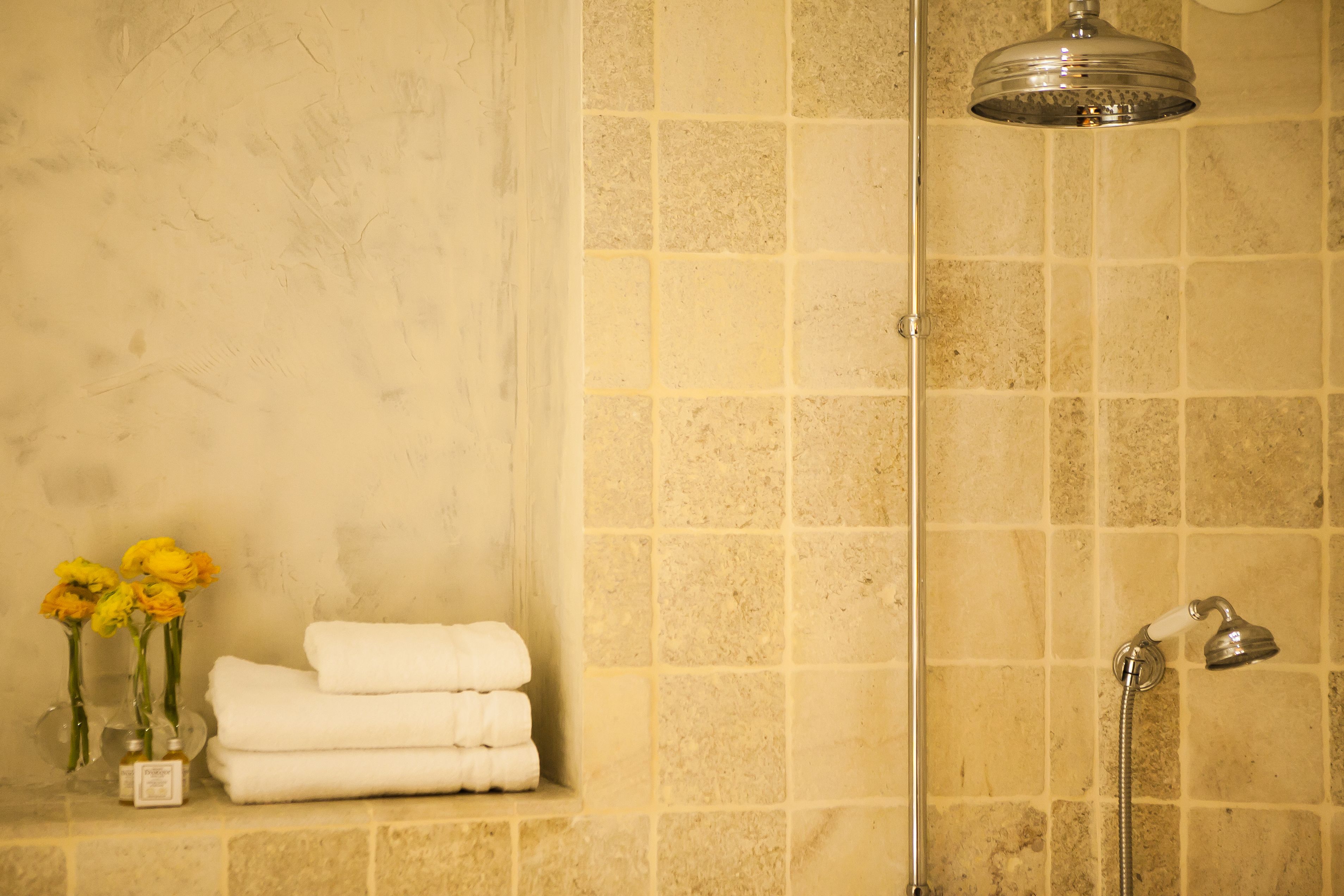 Un baño con baldosas color beige, cabina de ducha de vidrio, toallas blancas y flores amarillas.