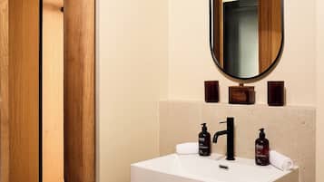 Un baño con un lavamanos blanco, un grifo negro y un espejo encima. Hay dos jabones en el lavamanos.