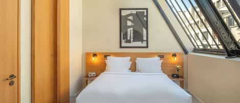 A hotel room with a bed, two bedside tables, a framed picture on the wall, and a window with a view of buildings.
