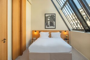A hotel room with a bed, two bedside tables, a framed picture on the wall, and a window with a view of buildings. - Maison Honnel (Paris)