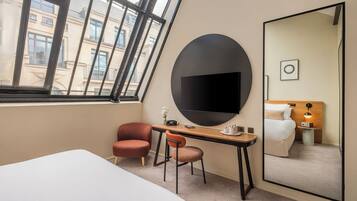 Habitación de hotel con cama, escritorio, dos sillas, un espejo grande y televisor.