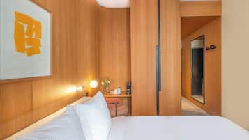 Habitación de hotel con cama, mesita de noche, espejo y lámpara de pared.