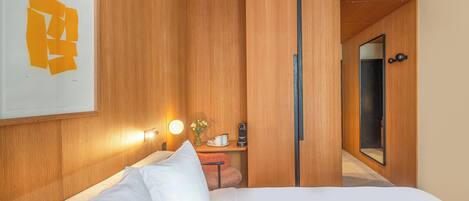 A hotel room with a bed, a nightstand, a mirror, and a wall-mounted light fixture.