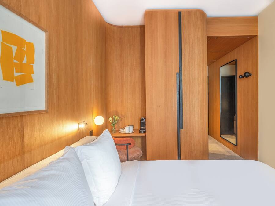 Habitación de hotel con cama, mesita de noche, espejo y lámpara de pared.