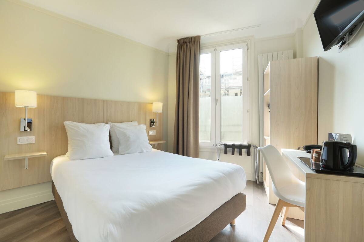 A hotel room with a large bed, a desk with a chair, a television, and a window with curtains.