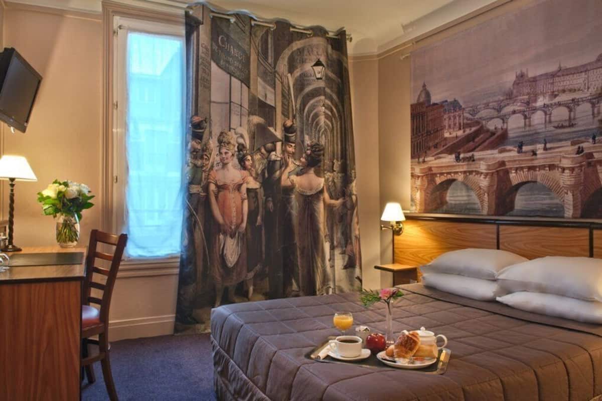 A hotel room with a bed, a desk, a chair, a painting of a bridge, and a curtain with a historical scene.