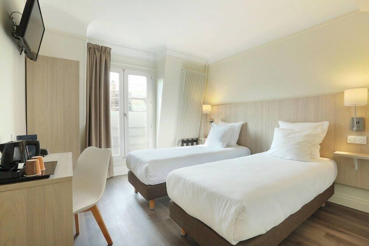 Habitación de hotel con dos camas, un escritorio con computadora, una silla y un televisor montado en la pared.